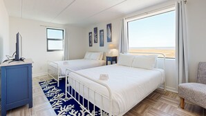 Habitación de hotel con dos camas, un escritorio, una lámpara y vista a la playa.