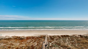 Una playa con un paseo marítimo de madera que conduce a la orilla, arena y océano.