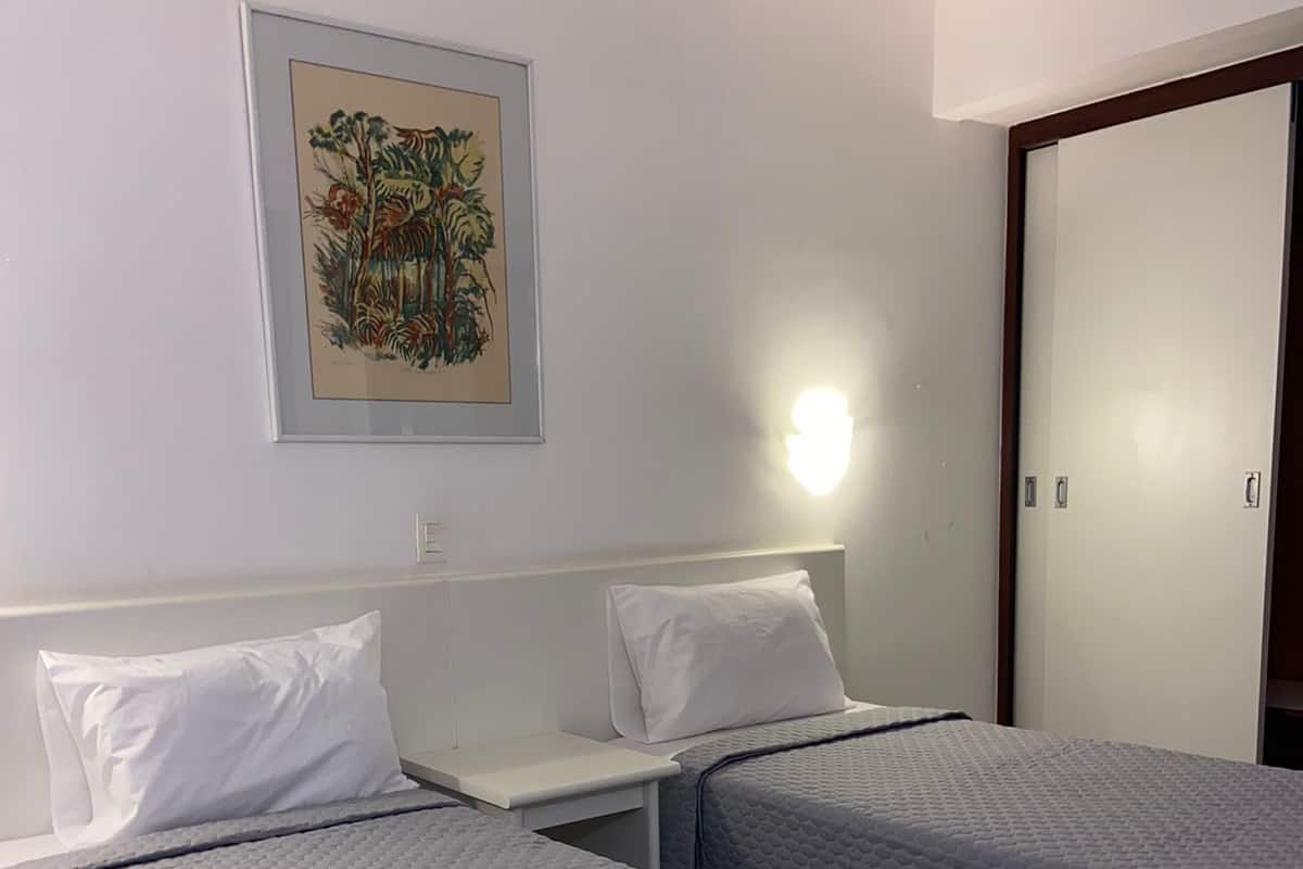 A hotel room with two single beds, a nightstand, a wall-mounted light, and a door.