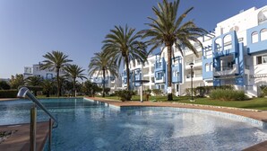 Una piscina con bordeado de azulejos, rodeada de palmeras y un edificio con paredes exteriores azules y blancas.