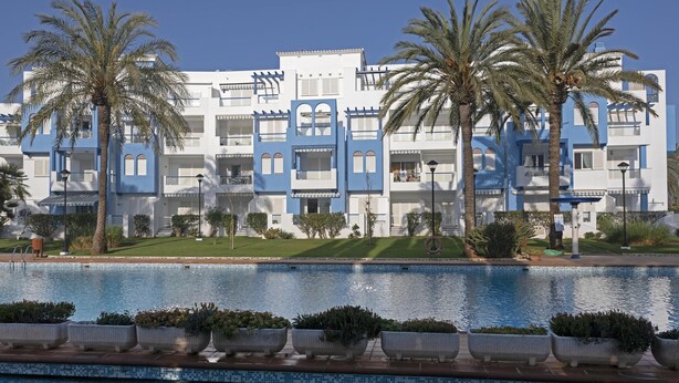 Un hotel con piscina, palmeras y fachada azul y blanca.