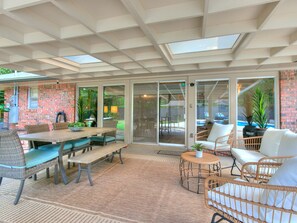 A covered patio area with a brick wall, wicker furniture, and a large sliding glass door leading to a backyard. - Poppy's Place - Campus Home w/ Pool (Norman)