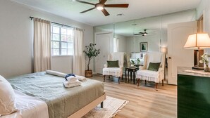 Ein Schlafzimmer mit einem Bett, zwei Stühlen, einem kleinen Tisch, einem Spiegel und einem Deckenventilator.