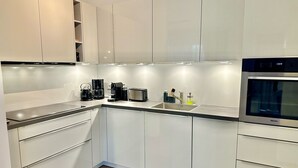 A modern kitchen with white cabinets, a stainless steel oven, a coffee maker, and a toaster. - 2802 Wohnung 2 - 2802 - Strandwiese 14 - Wohnung 2 (Dahme)