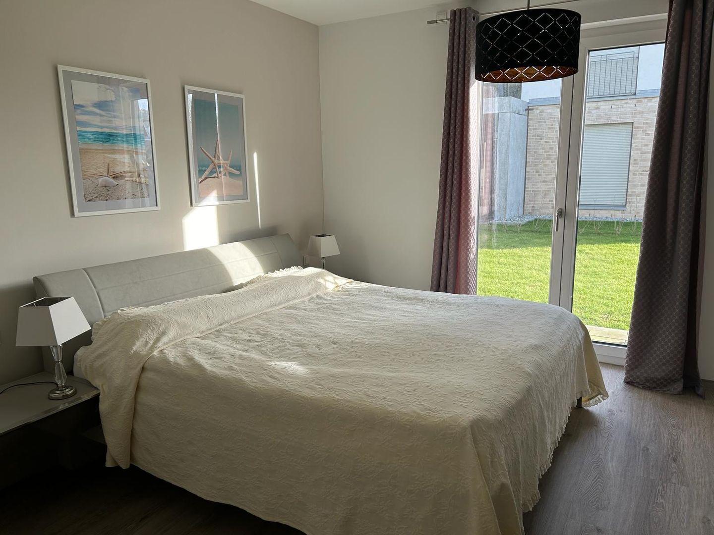 Et soveværelse med seng, natbord, lampe og et vindue med gardiner.