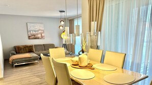 A modern dining area with a wooden table, chairs, and a sofa in the background. - 2802 Wohnung 2 - 2802 - Strandwiese 14 - Wohnung 2 (Dahme)