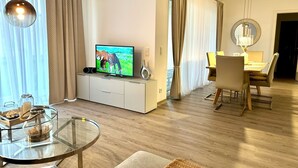 A modern living room with a flat-screen TV, a glass coffee table, and a dining area with a table and chairs. - 2802 Wohnung 2 - 2802 - Strandwiese 14 - Wohnung 2 (Dahme)