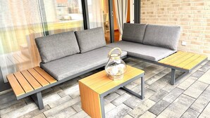 A modern outdoor seating area with a sofa, two wooden tables, and a glass container. - 2802 Wohnung 2 - 2802 - Strandwiese 14 - Wohnung 2 (Dahme)
