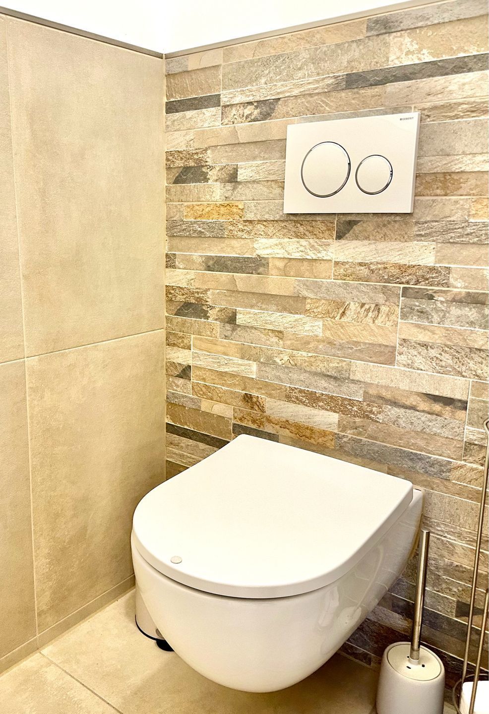A bathroom with a toilet, a wall-mounted air conditioning unit, and a toilet brush.