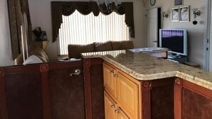 A kitchen with wooden cabinets, a granite countertop, a built-in stove, and a window with curtains. - Red Carpet Inn (Daytona Beach)