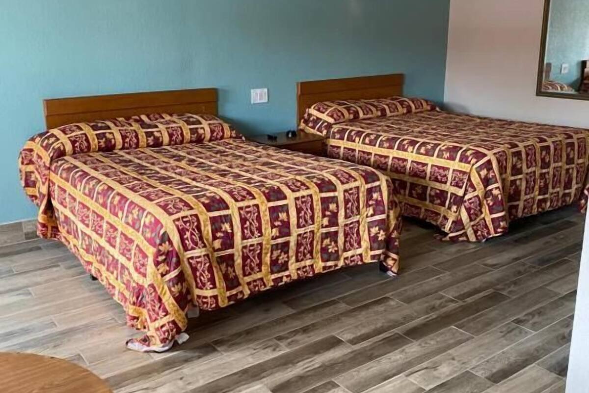 Une chambre d’hôtel avec deux lits, une table ronde en bois et un miroir au mur.