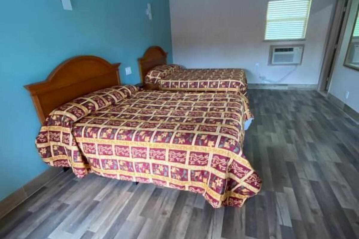 Une chambre avec deux lits, une fenêtre avec des stores et un système de climatisation intégré.