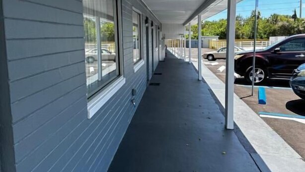 A covered corridor with a dark floor, large windows on one side, and a parking area with cars on the other. - Red Carpet Inn (Daytona Beach)