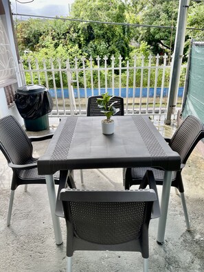 Relax in this serene outdoor space with a table and four comfortable chairs, surrounded by lush greenery and a charming picket fence.