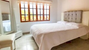 Une chambre à coucher avec un lit, une commode, un miroir et une fenêtre avec des stores.