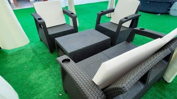 Un ensemble de meubles en osier avec des coussins, comprenant une chaise et une petite table, posé sur un tapis vert.