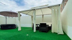 Un espace extérieur abrité, doté d’une pelouse artificielle, d’une table, de chaises et d’un grand parasol.