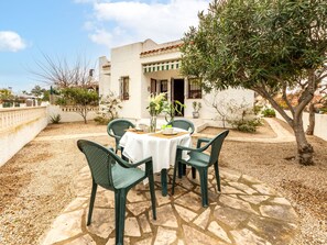 A patio with a table set for four, surrounded by green chairs, in front of a white building with a tiled roof. - Tu y Yo by Interhome (Deltebre)