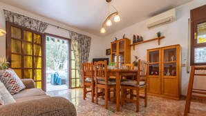 A cozy living room with a sofa, dining table, and chairs. There is a large window with curtains, a ceiling light, and a cabinet with glass doors. - Tu y Yo by Interhome (Deltebre)