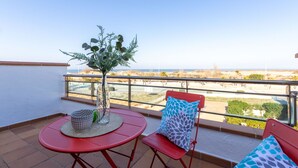 Uma varanda com mesa e cadeiras vermelhas, um vaso com planta e vista para a praia e o oceano.