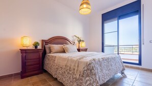 Quarto com uma cama grande, duas luminárias de cabeceira, uma mesa de cabeceira e vista para o exterior por uma grande janela.