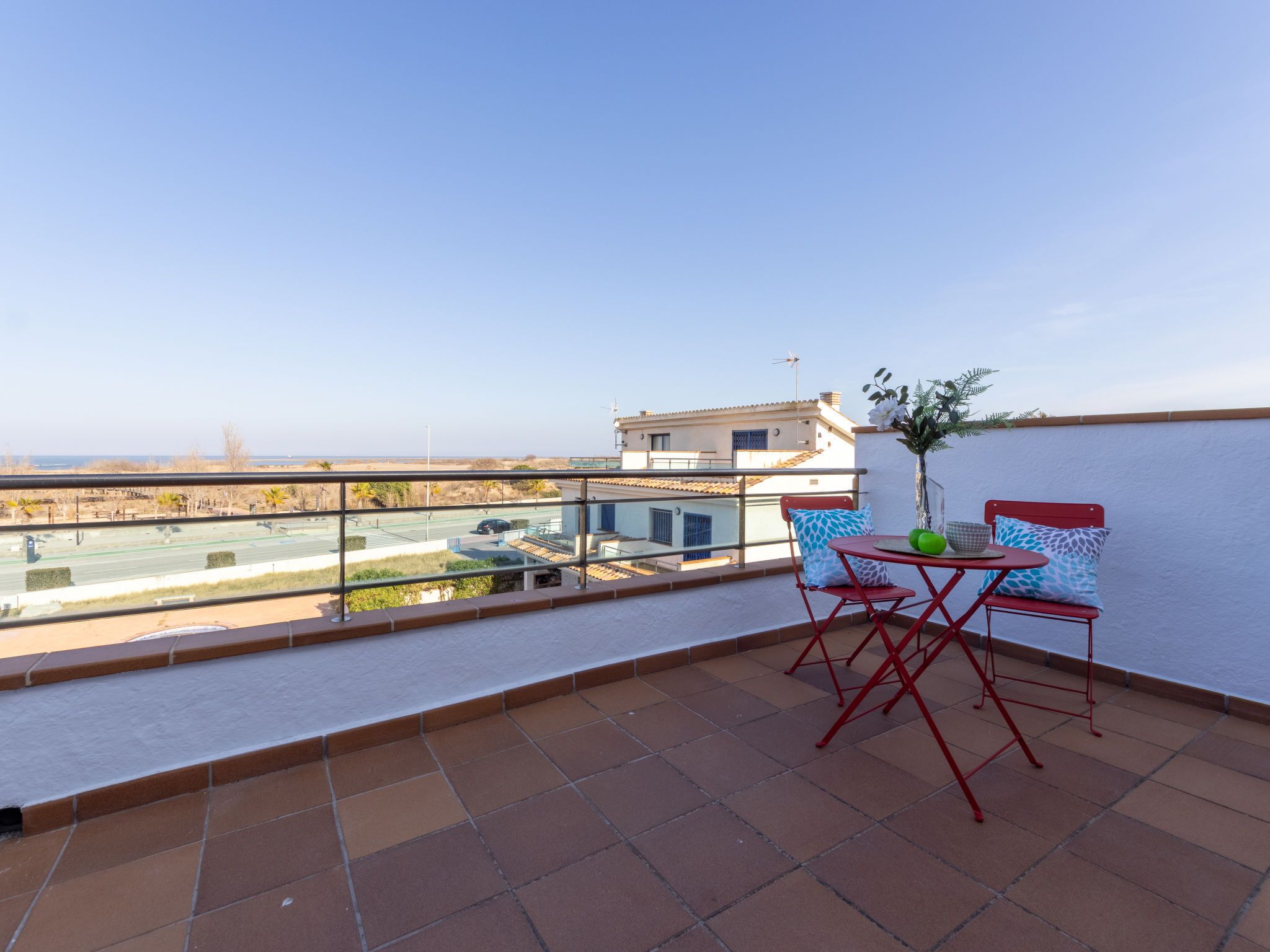 A balcony with a table and chairs, a view of a road and buildings, and a clear sky.