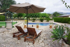A stone patio with two wooden lounge chairs and a large umbrella, a swimming pool, and potted plants. - 1 bedroom villa with private pool and barbecue (Moscari)