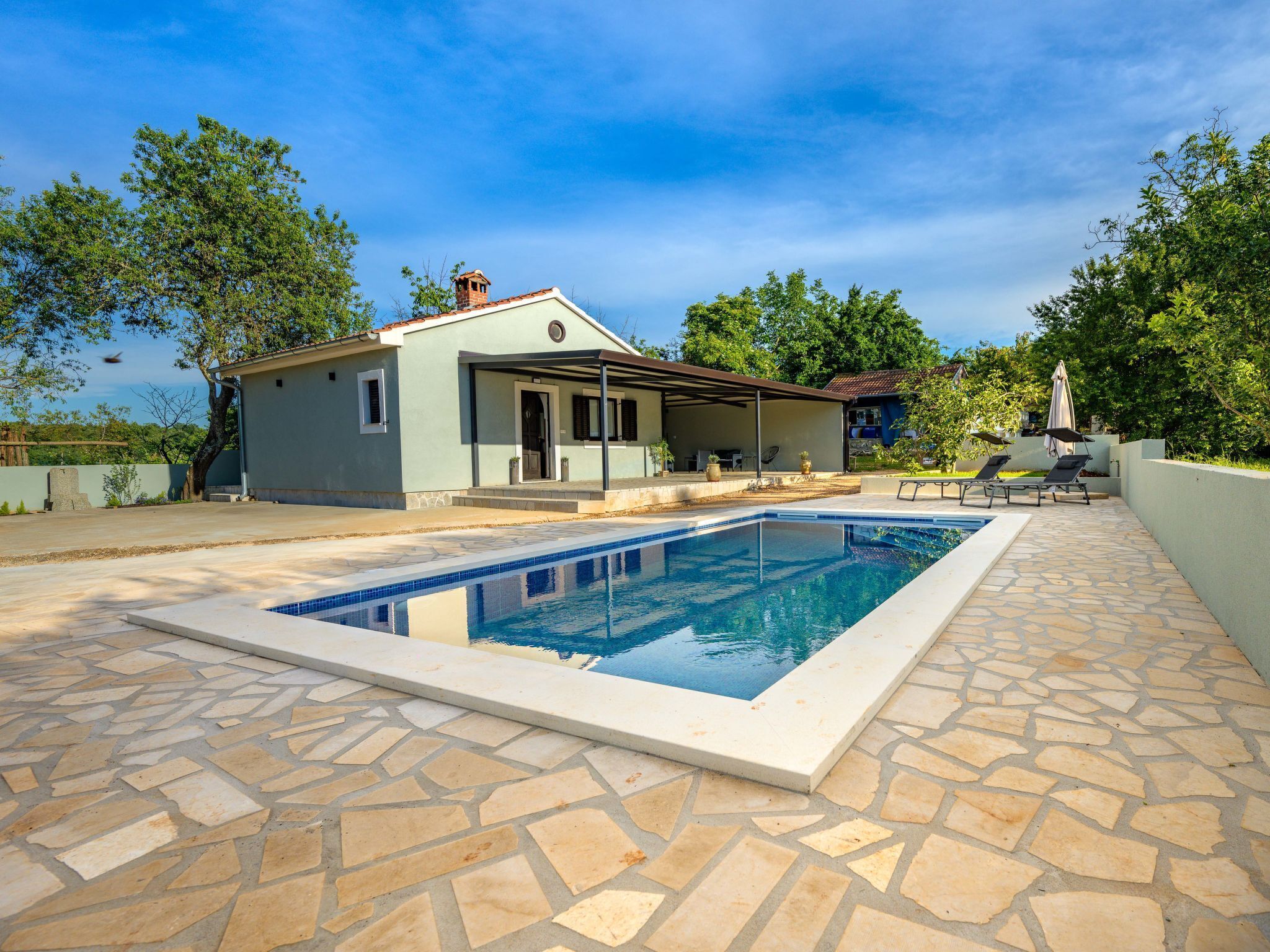 A swimming pool with a stone deck, a covered patio, and a house with a chimney.