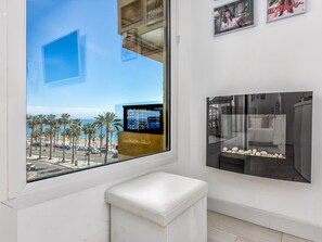 Un salón moderno con un amplio ventanal que da a una playa, un sofá blanco y un cuadro en la pared.