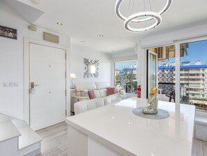 Un salón moderno con un sofá blanco, una mesa de comedor y vistas a la ciudad a través de amplios ventanales.