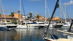 Un port de plaisance avec des bateaux amarrés, un ciel dégagé et des bâtiments en arrière-plan.