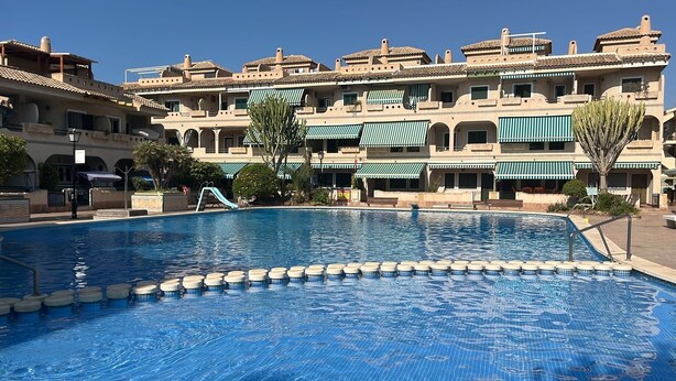 Une piscine dotée d’une terrasse carrelée, entourée d’un bâtiment comportant de nombreux balcons et des auvents verts.