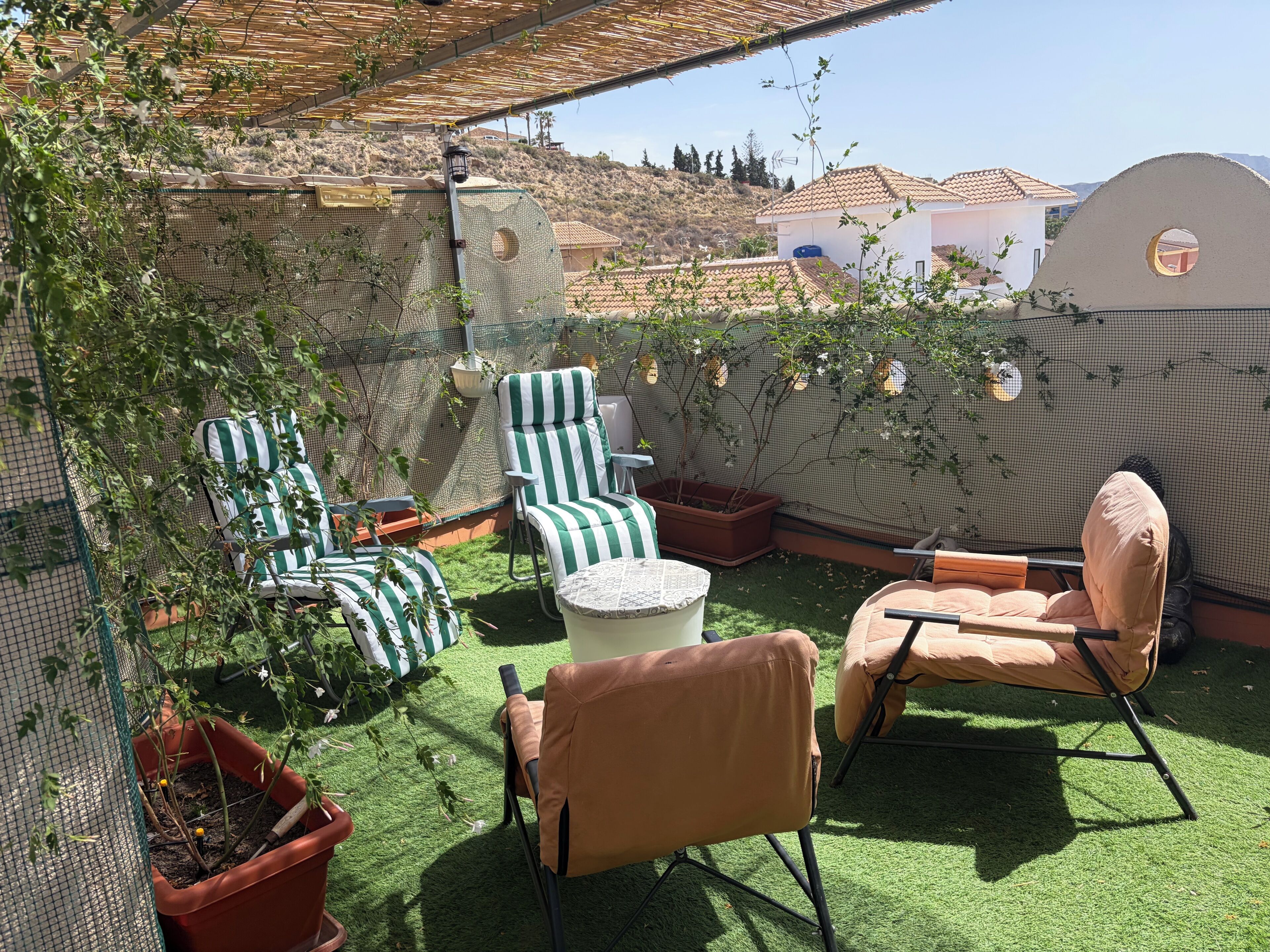 A patio with green artificial grass, two striped chairs, a round table, and potted plants.
