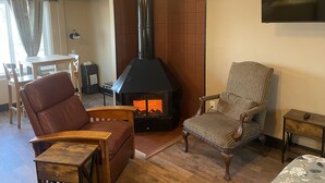 Una sala de estar con chimenea, un sofá, un sillón, un televisor montado en la pared y un ventilador de techo.