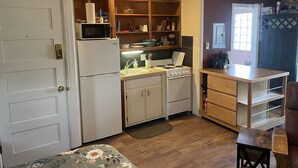 Una cocina compacta equipada con refrigerador, microondas, pileta, estufa y alacenas de madera.