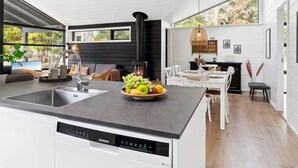 A modern kitchen with a built-in dishwasher, a dining area with white furniture, and a large window offering a view of greenery. - "Ela" - 800m from the sea by Interhome (Vig)