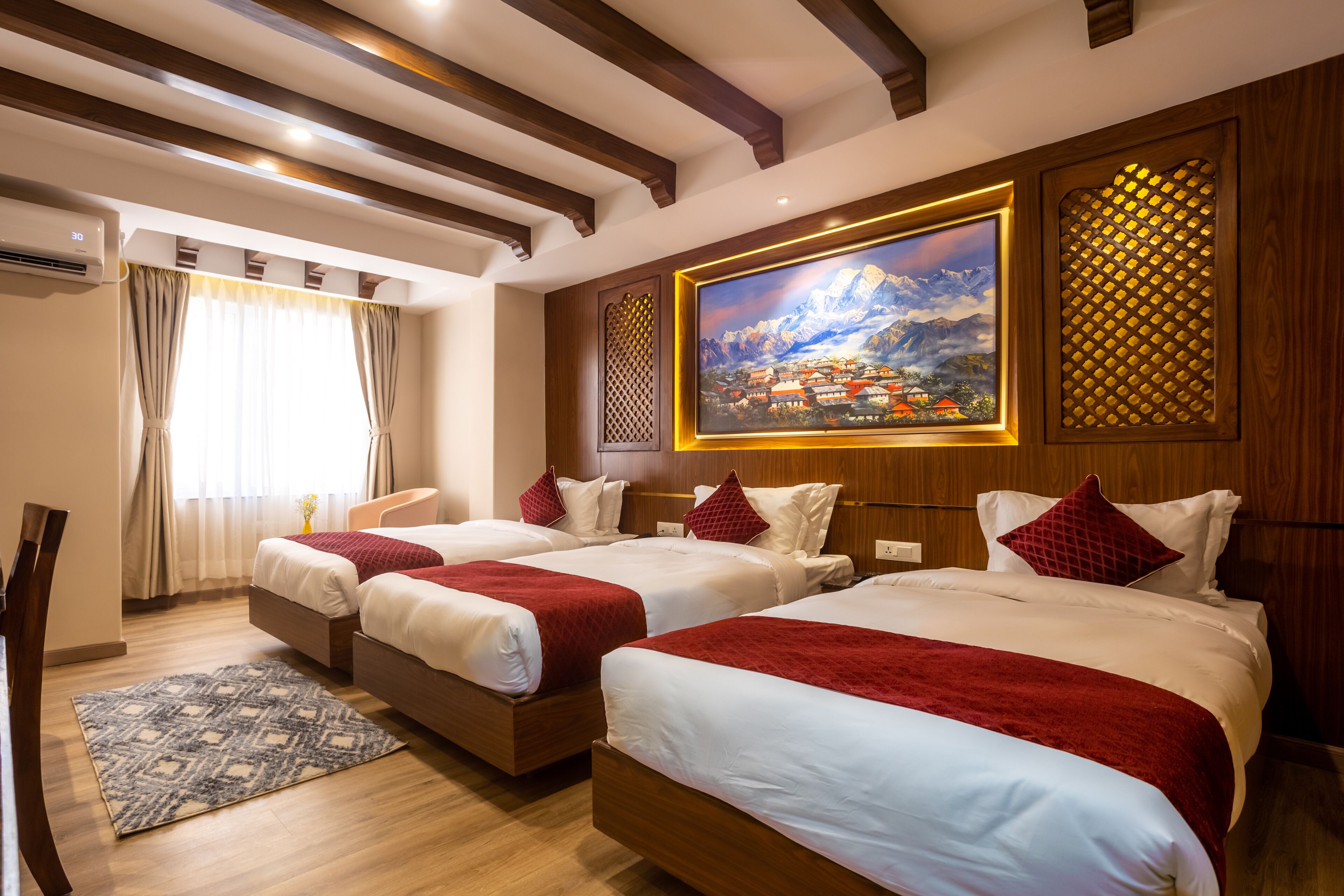 A hotel room with three beds, a painting of a mountain landscape, wooden paneling, and a patterned rug.