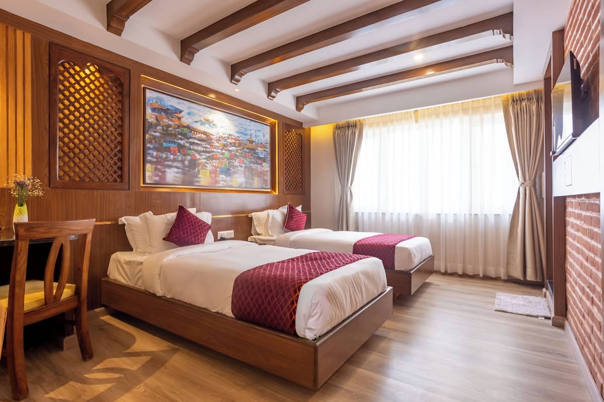 Ein Hotelzimmer mit zwei Betten, Holzmöbeln, einem Bild an der Wand und einem Fenster mit Vorhängen.