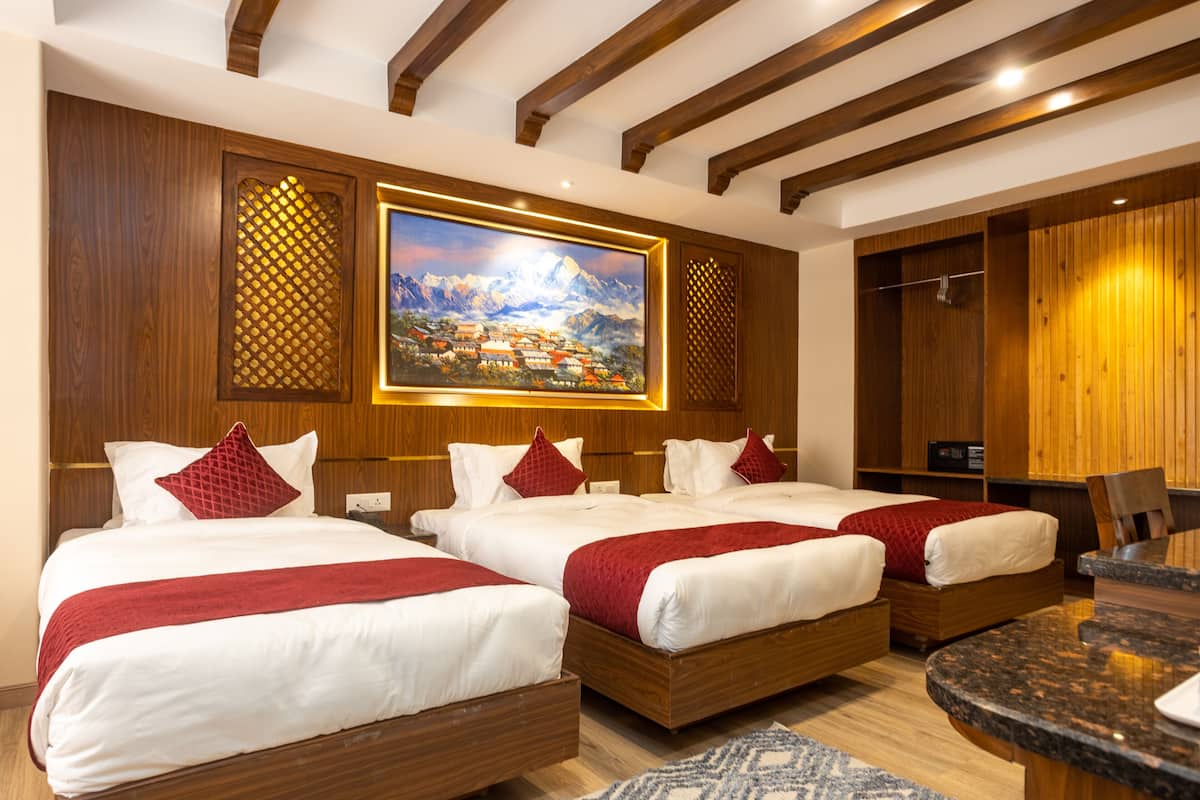 Ein Hotelzimmer mit drei Betten, einem Gemälde einer Berglandschaft, Holzvertäfelung und einem Essbereich mit Tisch und Stühlen.