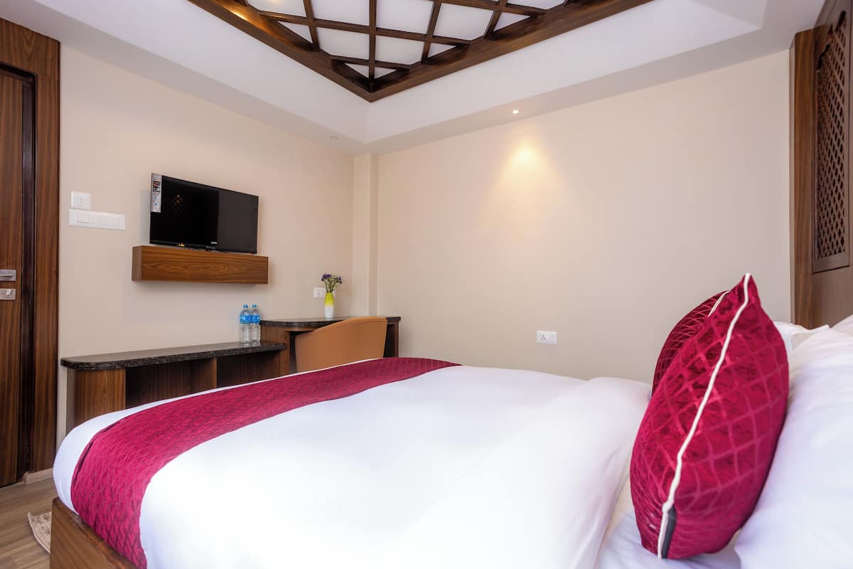 Ein Hotelzimmer mit Bett, Schreibtisch, Flachbildfernseher, Wasserflasche und Blumen in einer Vase.