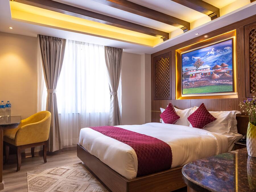 Habitación de hotel con una cama grande, un escritorio con silla, un cuadro en la pared y una ventana con cortinas.