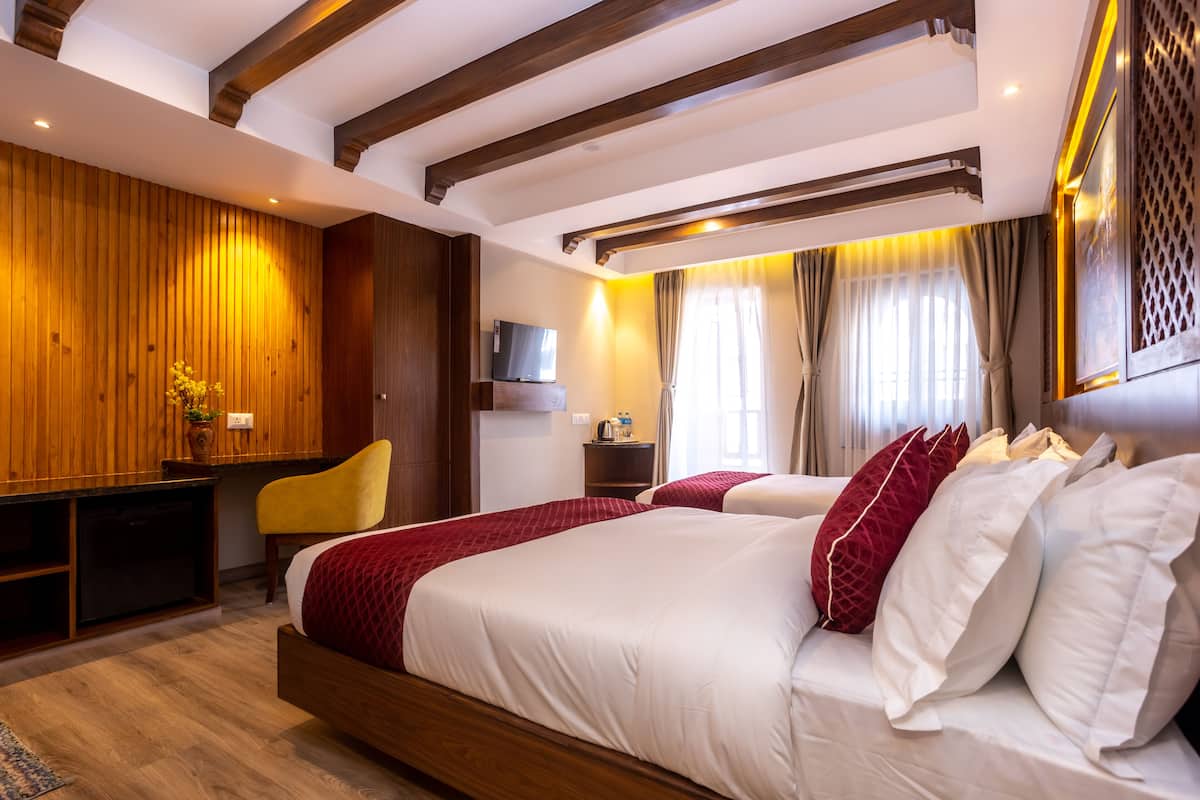 Ein modernes Hotelzimmer mit Holzboden, einem großen Bett mit weißer und roter Bettwäsche, einem Schreibtisch mit Stuhl und einem Fernseher an der Wand.