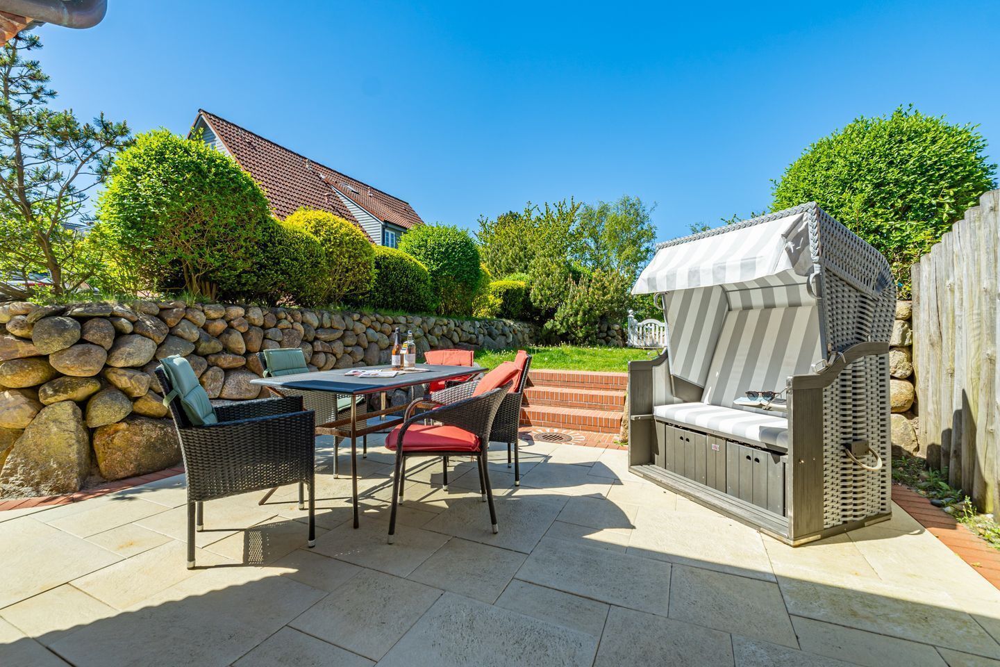 A patio with a stone wall, a table with chairs, and a barbecue grill.