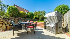 A patio with a stone wall, a table with chairs, and a barbecue grill. - Senmare - Geschmackvolles Ferienhaus für Sechs Personen in Wattnähe!! (Sylt)