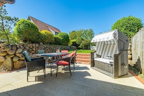 Eine Terrasse mit Steinmauer, Tisch mit Stühlen und einem Grill.