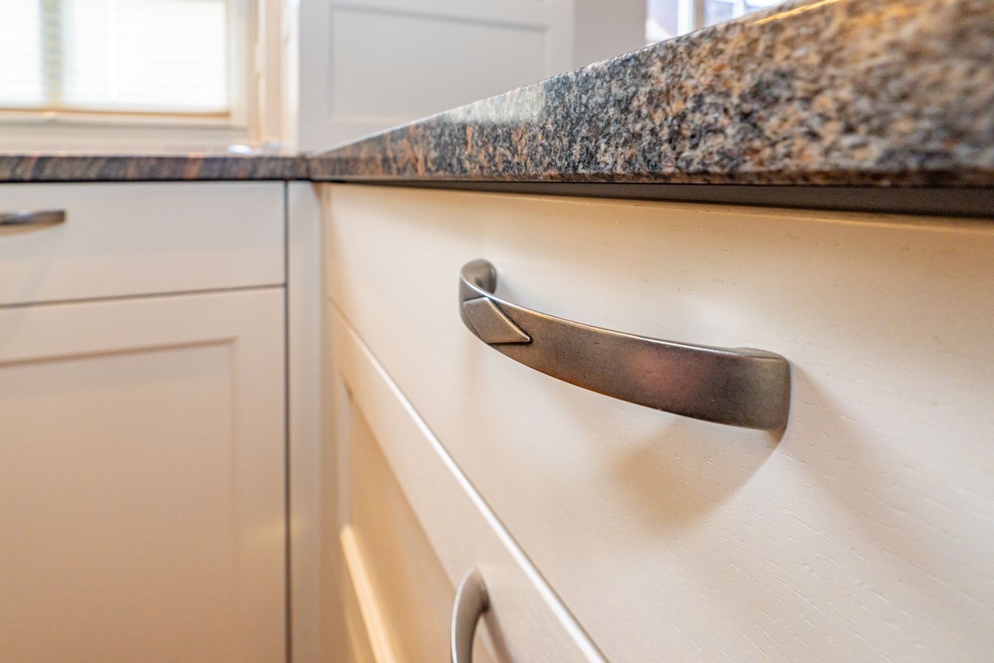 A kitchen with white cabinets, a granite countertop, and a stainless steel handle.