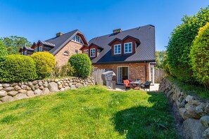 Una casa de dos pisos con un muro de contención de piedra, un patio con mobiliario exterior y un jardín bien cuidado.