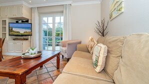 A living room with a beige sofa, a wooden coffee table, a television on a cabinet, and a large window with curtains. - Senmare - Geschmackvolles Ferienhaus für Sechs Personen in Wattnähe!! (Sylt)