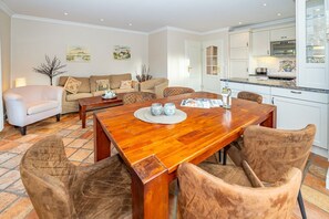 Un comedor con una mesa de madera y seis sillas, un sofá, y una cocina al fondo.