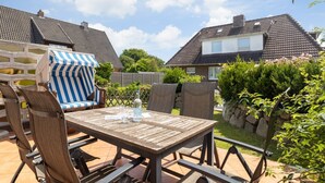 Eine Terrasse im Freien mit einem Holztisch und Stühlen, einem gestreiften Stuhl und einer Wasserflasche.